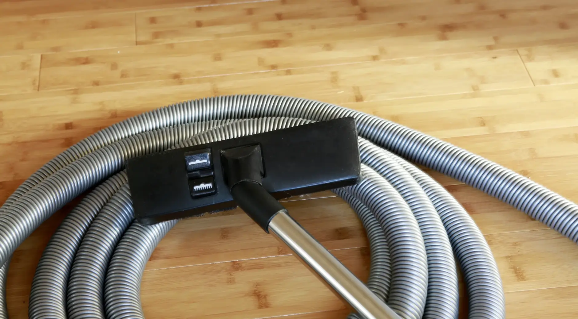 Central vacuum hose and floor brush attachment coiled on a hardwood floor