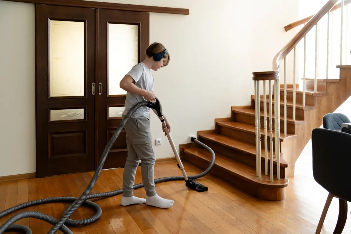 Person vacuuming hardwood floors with a central vacuum hose in a home entryway near a staircase